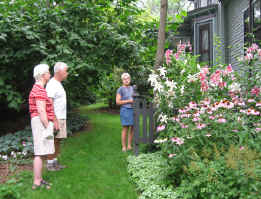 Picture of neighbors touring perennial bed with pink and white lillies, pink cone flowers, astilbe and silvery lamium edging the border